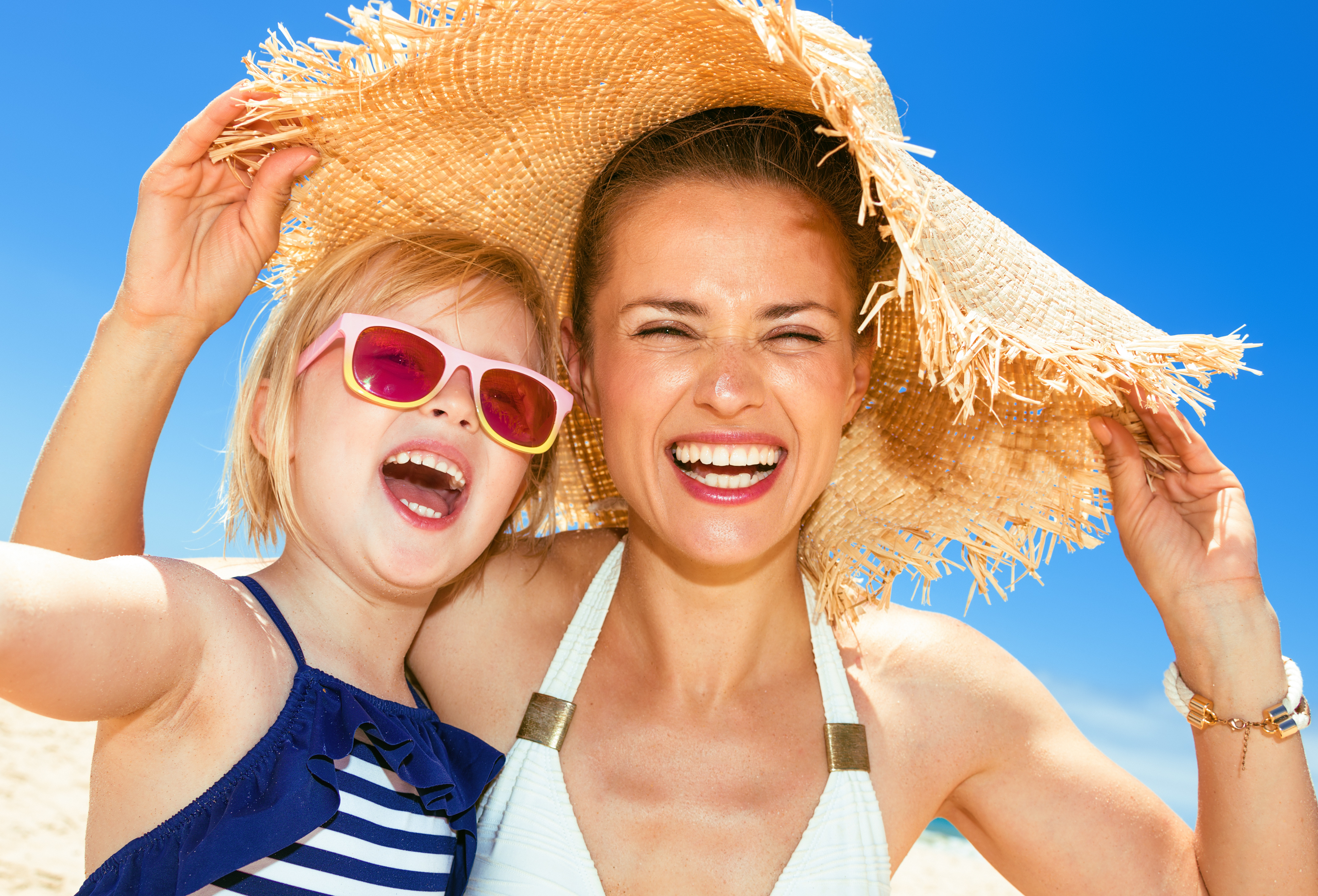 Family fun on white sand. happy modern mother and child in swimwear on the seacoast taking selfie