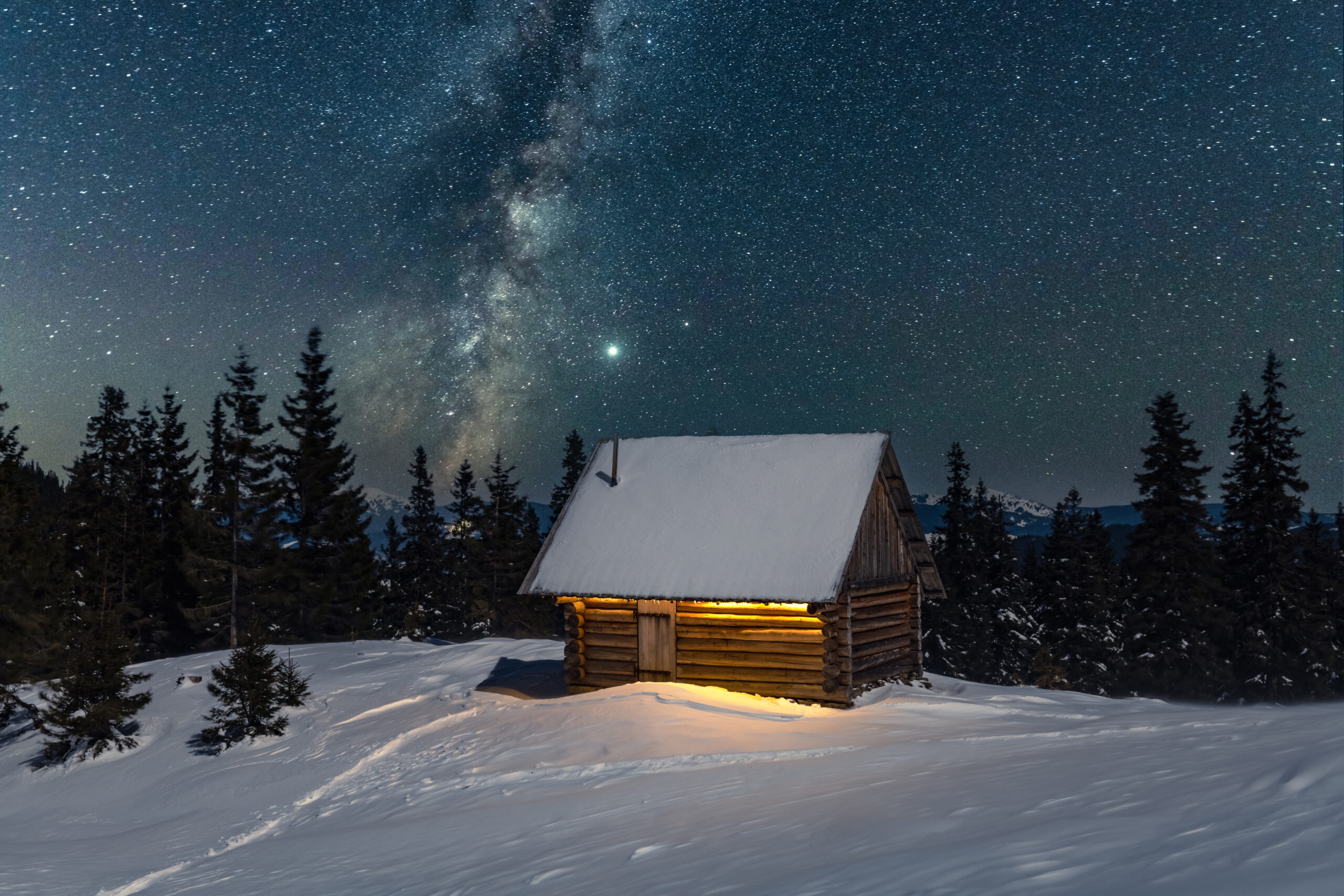 Fantastic winter landscape with wooden house in snowy mountains. Starry sky with Milky Way and snow covered hut. Christmas holiday and winter vacations concept